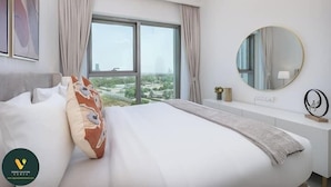 A modern hotel room with a large bed, a round mirror, and a view of a cityscape through a large window. - Vogue | Downtown with Direct Access to Dubai Mall (Dubai)