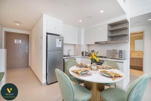 A modern kitchen with white cabinets, a stainless steel refrigerator, and a dining area with a round table and green chairs. - Vogue | Downtown with Direct Access to Dubai Mall (Dubai)