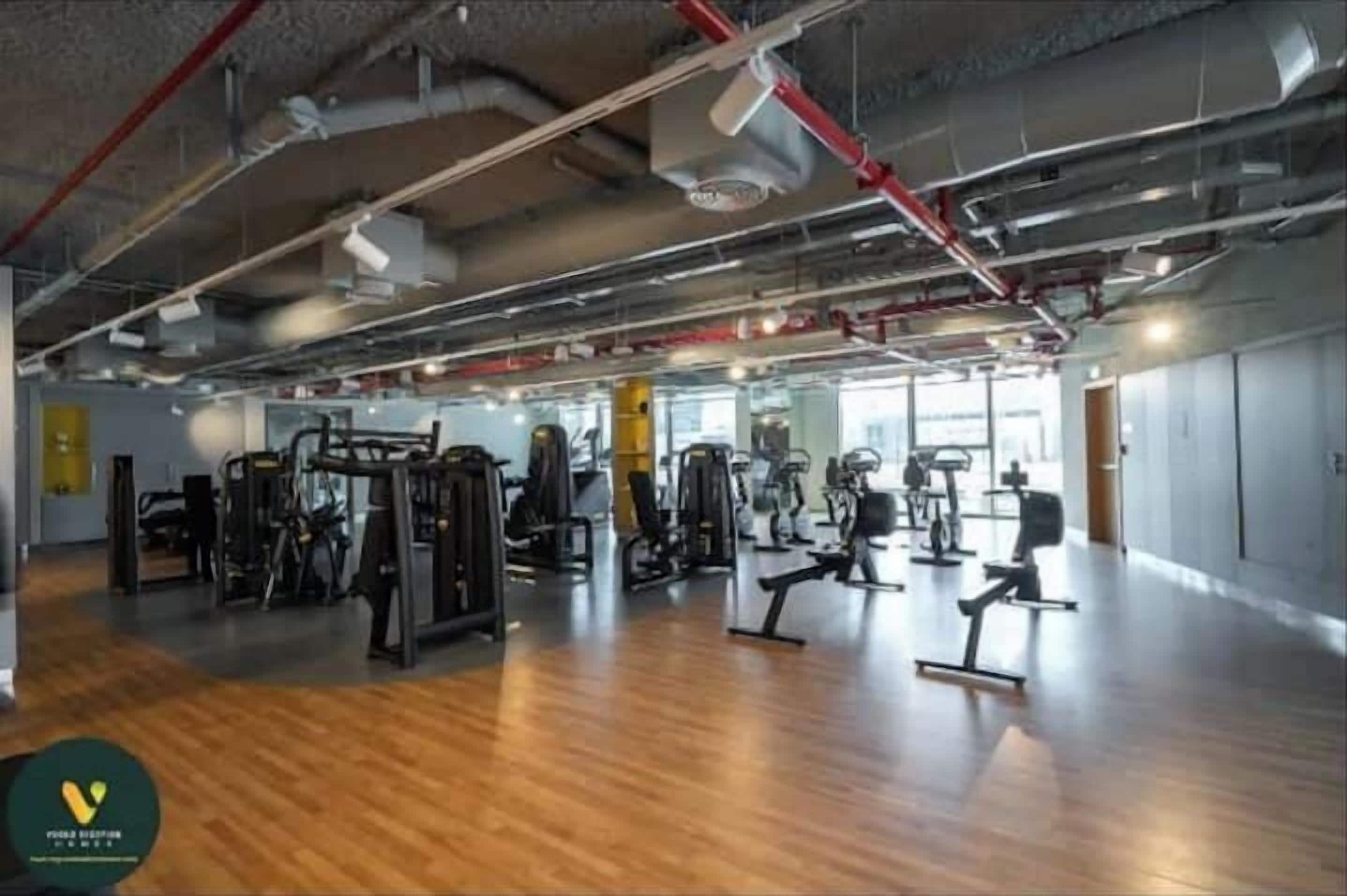 A spacious gym with various exercise equipment, wooden flooring, and visible ductwork on the ceiling.