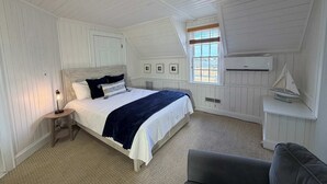 Un dormitorio con una cama, una mesita de noche, una ventana con persianas, un modelo de velero pequeño y un sofá gris.
