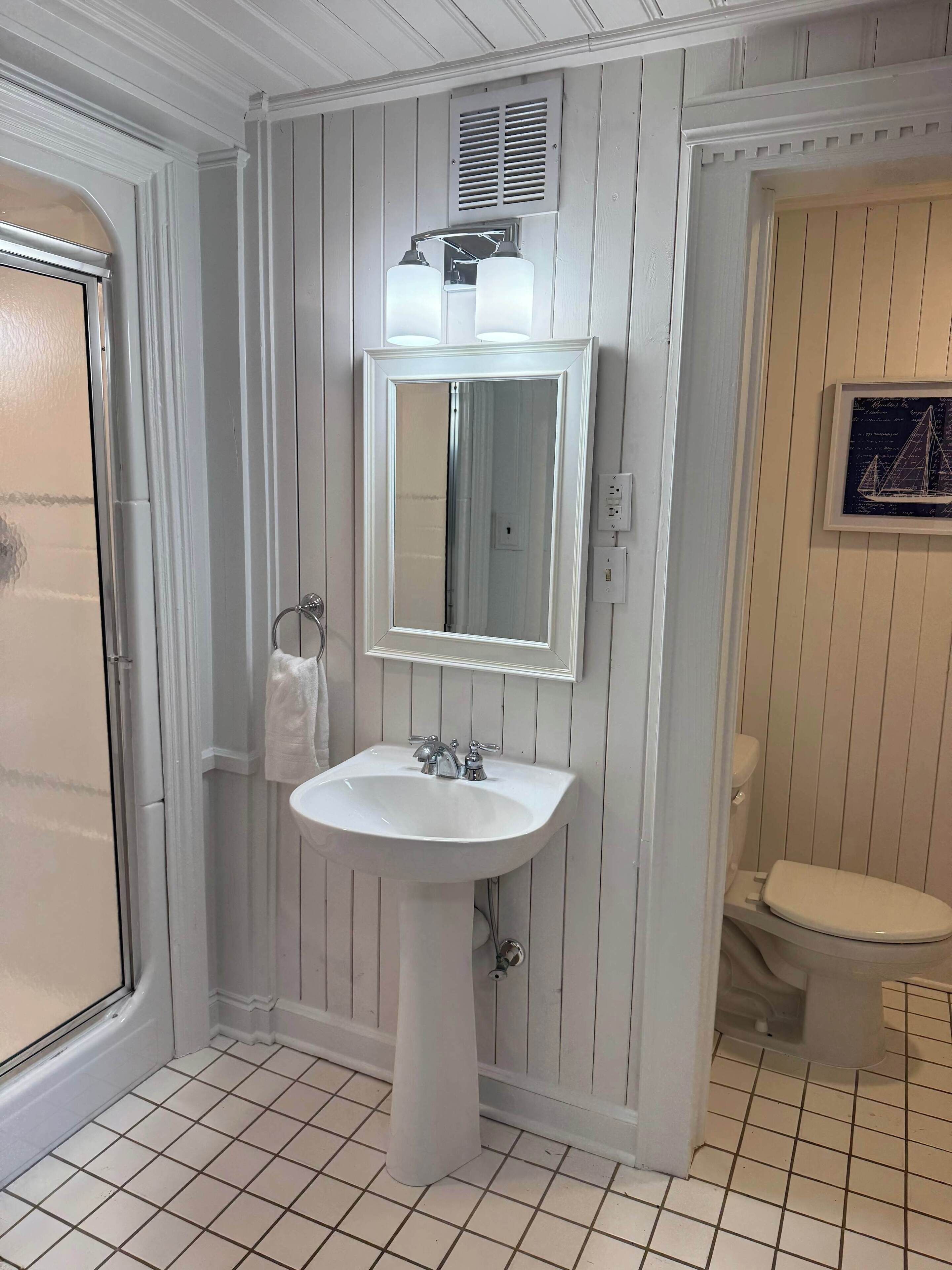 Un baño con lavamanos blanco, espejo, inodoro y zona de ducha.
