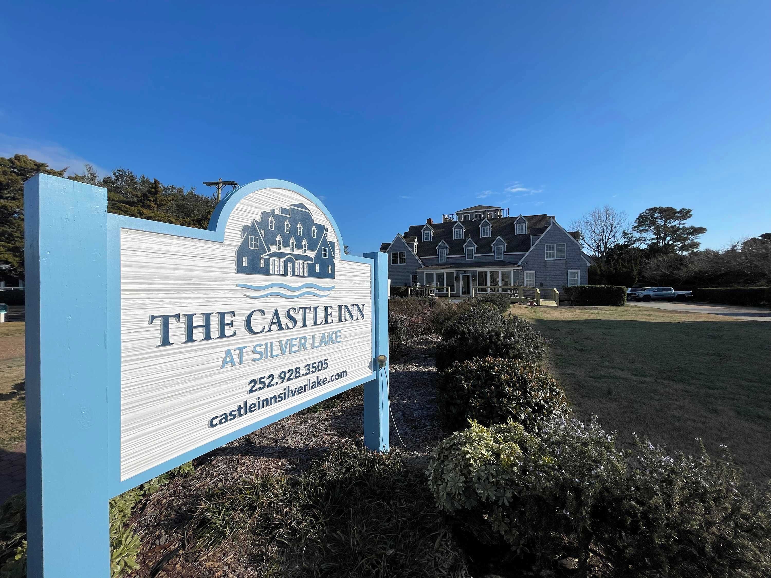 Un letrero de The Castle Inn en Silver Lake, con una casa grande al fondo.