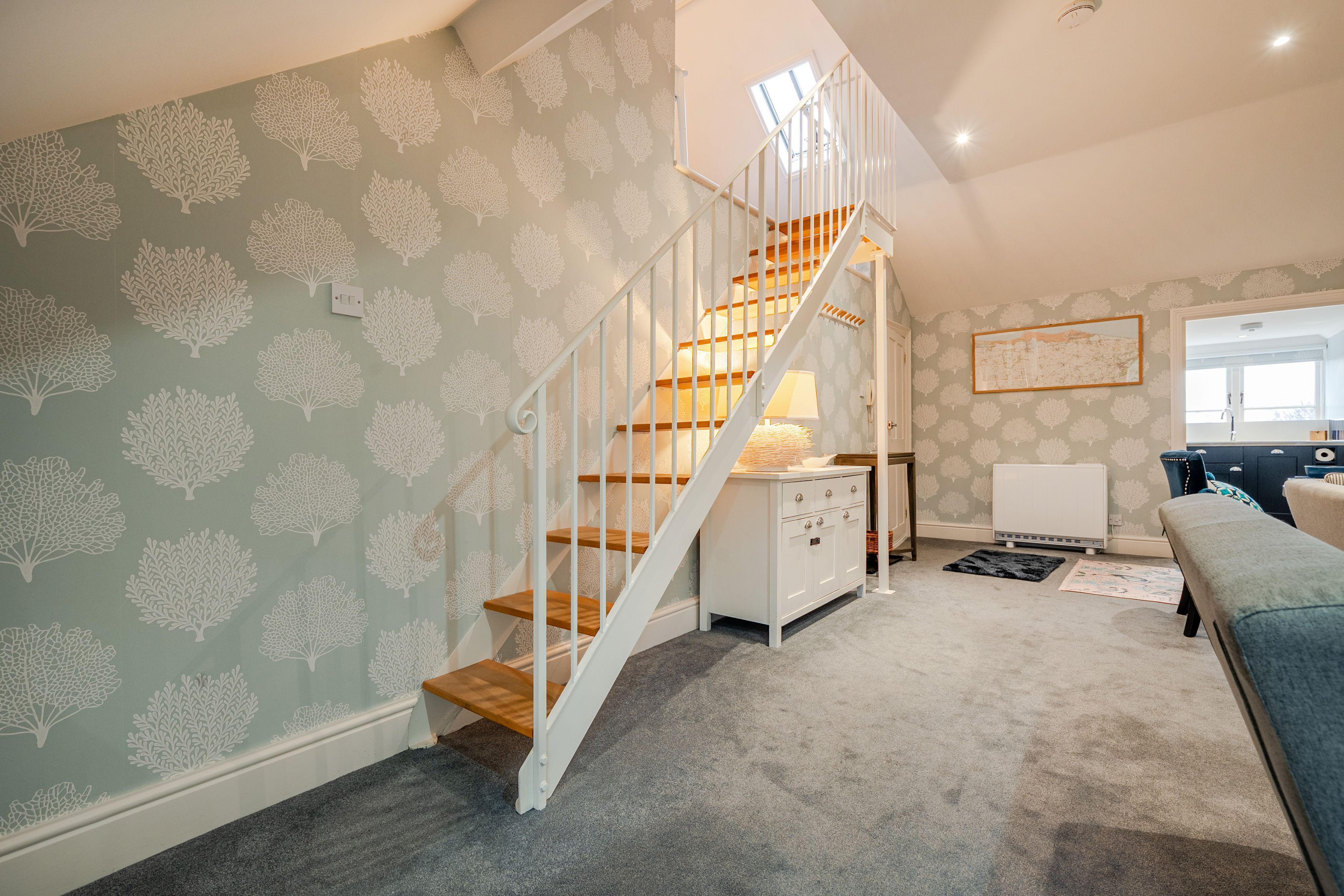 A staircase with white railings and wooden steps leading to a landing with a white cabinet and a lamp.