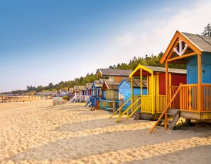 Eine Reihe bunter Strandhäuser mit Stufen, die zu ihnen hinaufführen, direkt am Sandstrand gelegen.