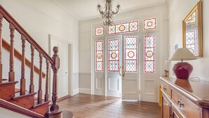 Una escalera de madera que conduce a una habitación con un candelabro, una alfombra estampada y un armario de madera con una lámpara.