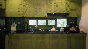 Una cocina con gabinetes verdes, encimera negra y ventana con vistas a la vegetación.
