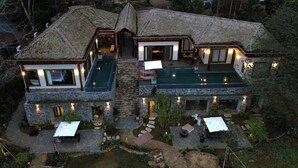 Una casa de dos pisos con fachada de piedra, piscina y zonas de estar al aire libre.