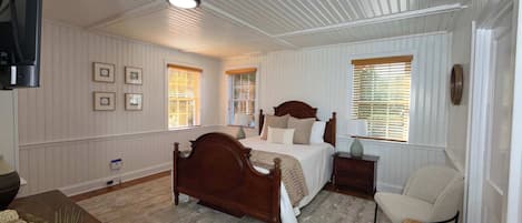 A bedroom with a wooden bed, two bedside tables, a chair, and a television mounted on the wall.