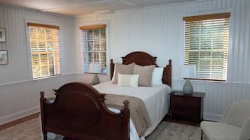 A bedroom with a wooden bed, white walls, and windows with blinds.