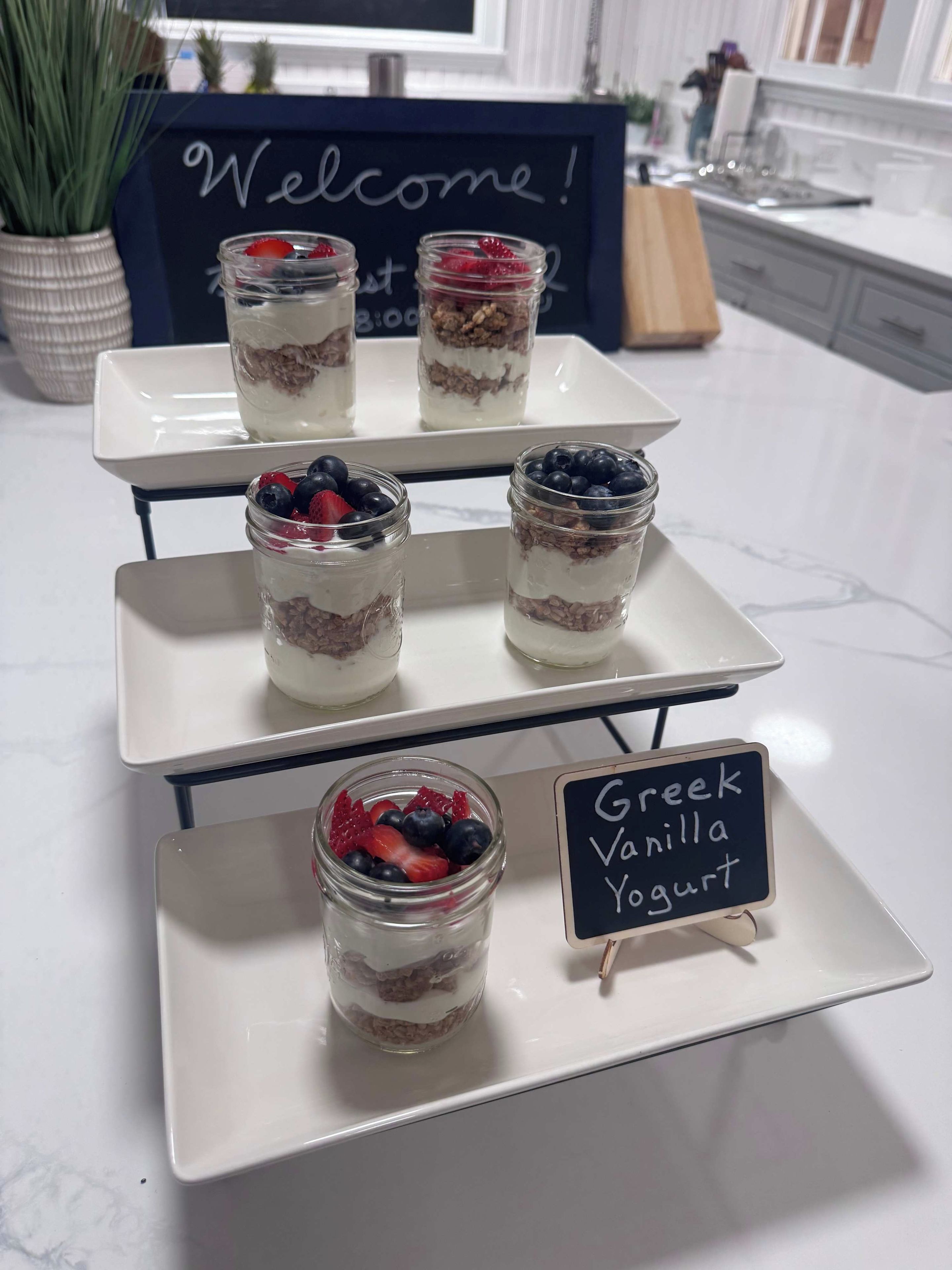 Una presentación de postres con parfait en capas y un cartel que indica yogur griego con vainilla.