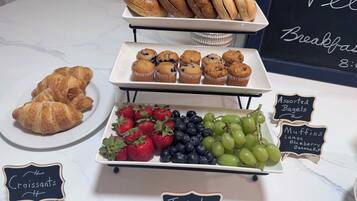 Un bufé de desayuno con croissants, muffins, bagels variados y fruta fresca.