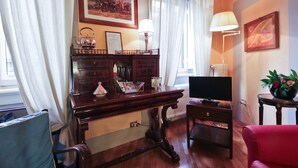 Una habitación con un escritorio de madera, televisión, una silla roja, lámpara y un cuadro en la pared.