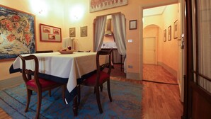 Un comedor con una mesa dispuesta para dos personas, un cuadro grande en la pared y vista a otra habitación.