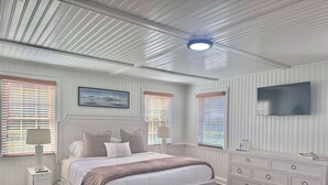 A bedroom with a bed, bedside tables, a dresser, a television, and a ceiling fan. - 04-The Seashell Suite at The Castle Inn (Ocracoke)