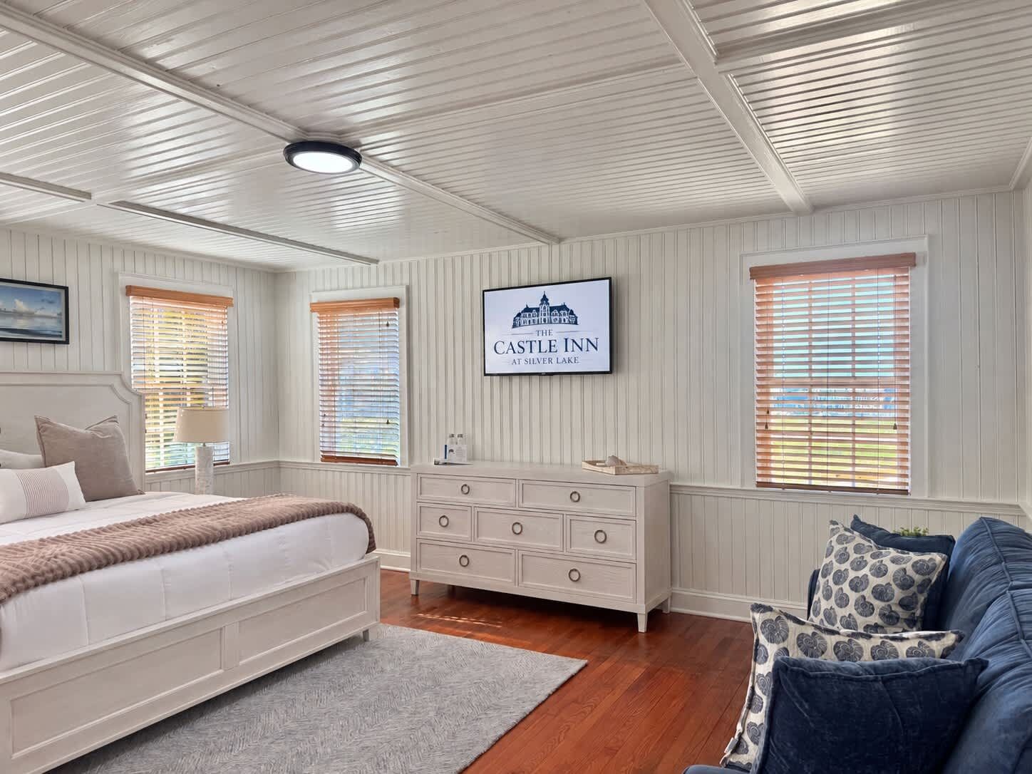 A bedroom with a bed, dresser, and a television displaying 'The Castle Inn at Silver Lake.'