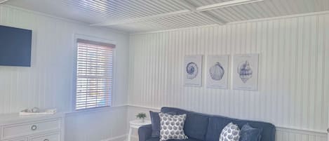 Una habitación con un sofá azul, un aparador blanco y una pequeña mesa blanca. Hay tres cuadros enmarcados en la pared.