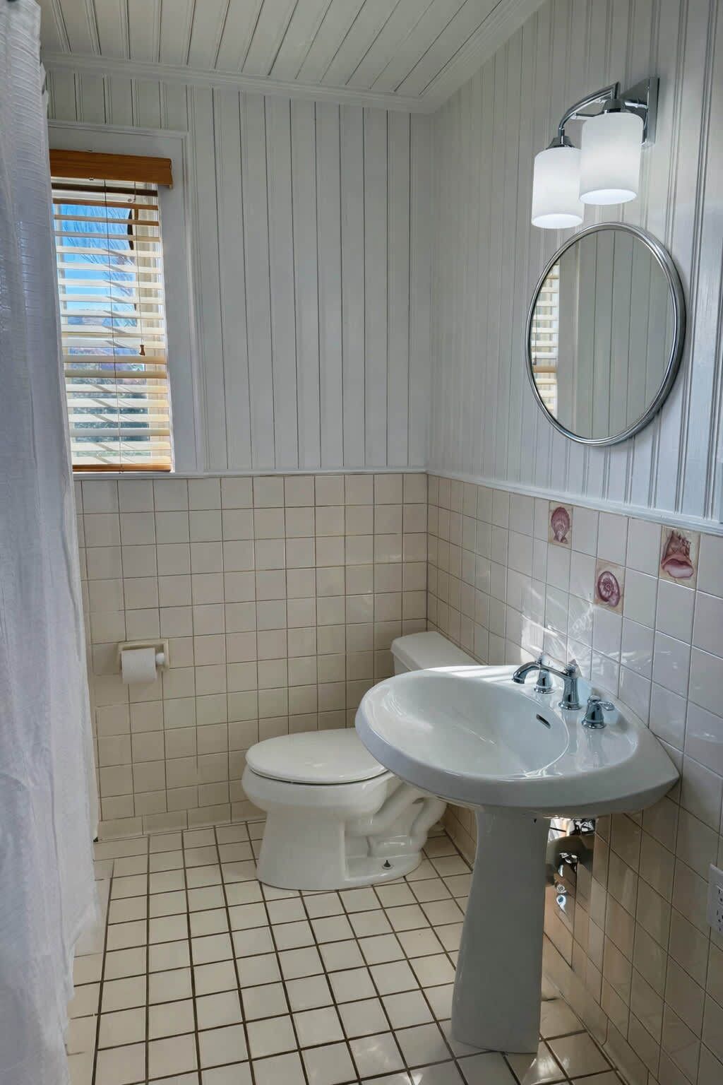 A bathroom with a toilet, sink, and window with blinds.
