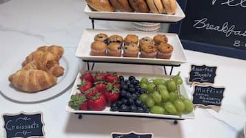 Un bufé de desayuno con croissants, muffins, bagels variados y fruta fresca.