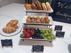 A breakfast buffet with croissants, muffins, assorted bagels, and fresh fruit.