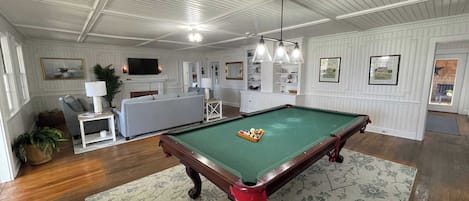 Una mesa de billar en una sala con sofá, televisor y chimenea.
