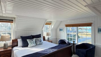 A bedroom with a large bed, a wooden headboard, a nightstand, a lamp, a chair, and a view of the outdoors through a window.