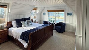 Une chambre avec un grand lit, une table de chevet, une chaise et une vue sur l’extérieur par une fenêtre.