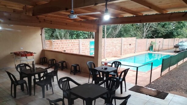 An outdoor patio area with tables and chairs, a pool, and a brick wall in the background. - Department 2 (Puerto Iguazú)