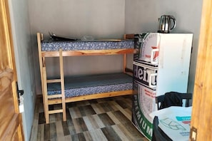 Una cama litera con un colchón estampado, una mesita con una tetera y un refrigerador con una cafetera encima.
