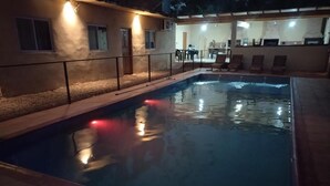 An outdoor swimming pool with a tiled deck, surrounded by a low fence. There are lounge chairs and a covered area with tables and chairs. - Department 2 (Puerto Iguazú)