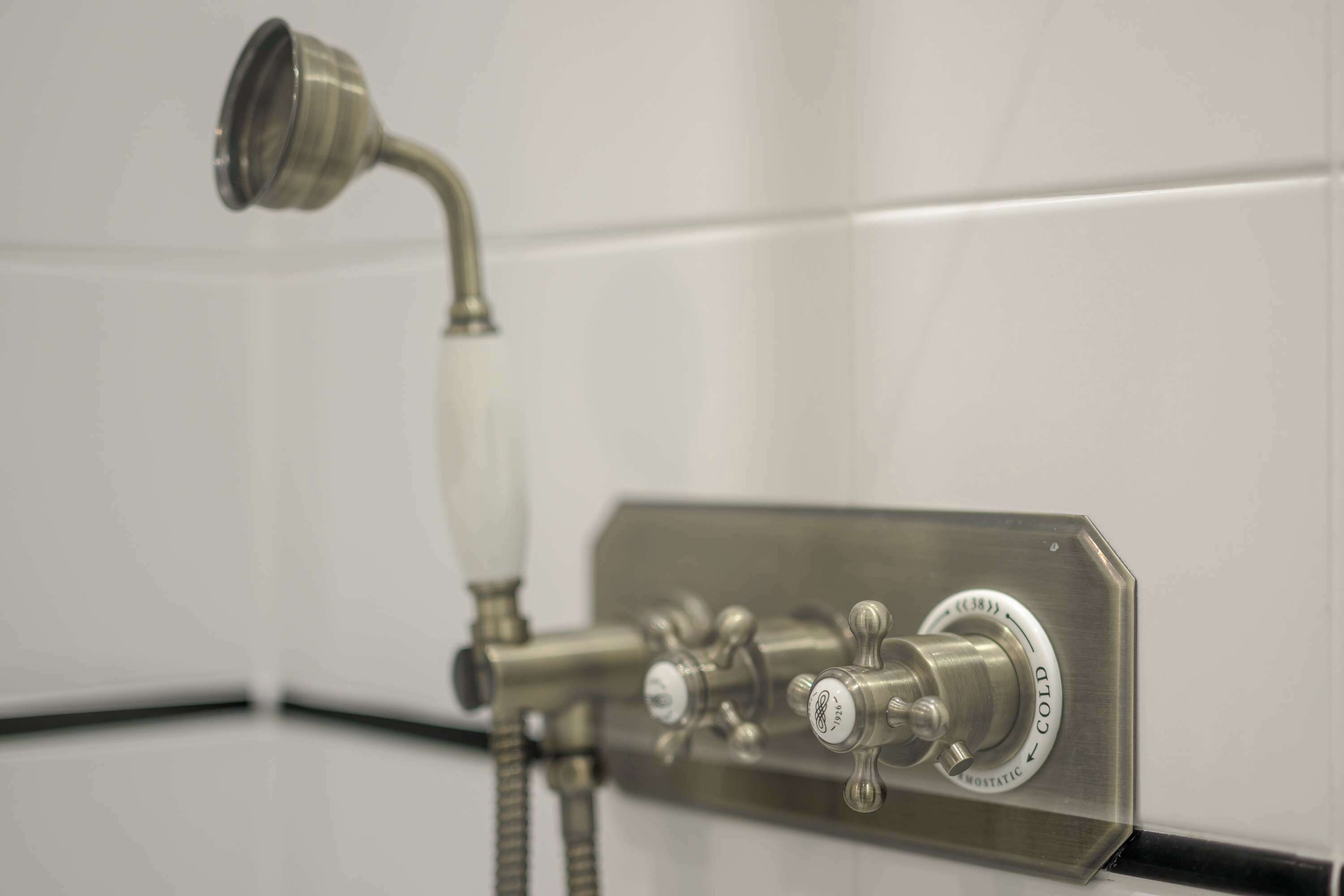 A shower with a handheld showerhead and a wall-mounted control panel with temperature and water flow settings.