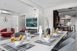 Ein stilvoller Essbereich mit einem langen Tisch, der für eine Mahlzeit gedeckt ist, einem roten Sofa und einem Gemälde einer Flusslandschaft an der Wand.