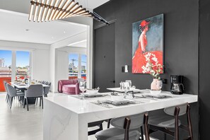 Een moderne keuken met een marmeren eiland, een eetgedeelte met grijze stoelen en een groot schilderij aan de muur.
