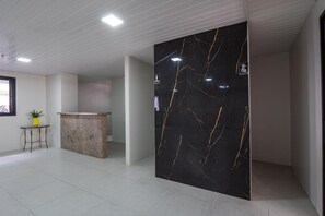 A modern reception area with a marble reception desk, a small table with a plant, and a black marble wall with gold veins. - Hamilton #1203 - Apto in Meirelles by Carpediem (Fortaleza)