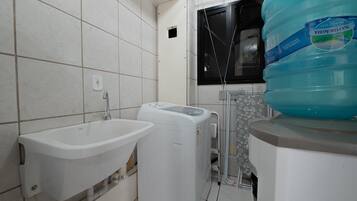 Un baño con lavamanos, lavadora y un dispensador de agua grande.