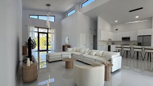 Ein großzügiger Wohnbereich mit einem modernen weißen Sofa, einem Couchtisch und Blick ins Freie durch große Fenster.