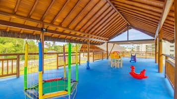 Uma área de lazer ao ar livre coberta, com piso azul, uma estrutura de recreação com tela e um cavalo de balanço vermelho.