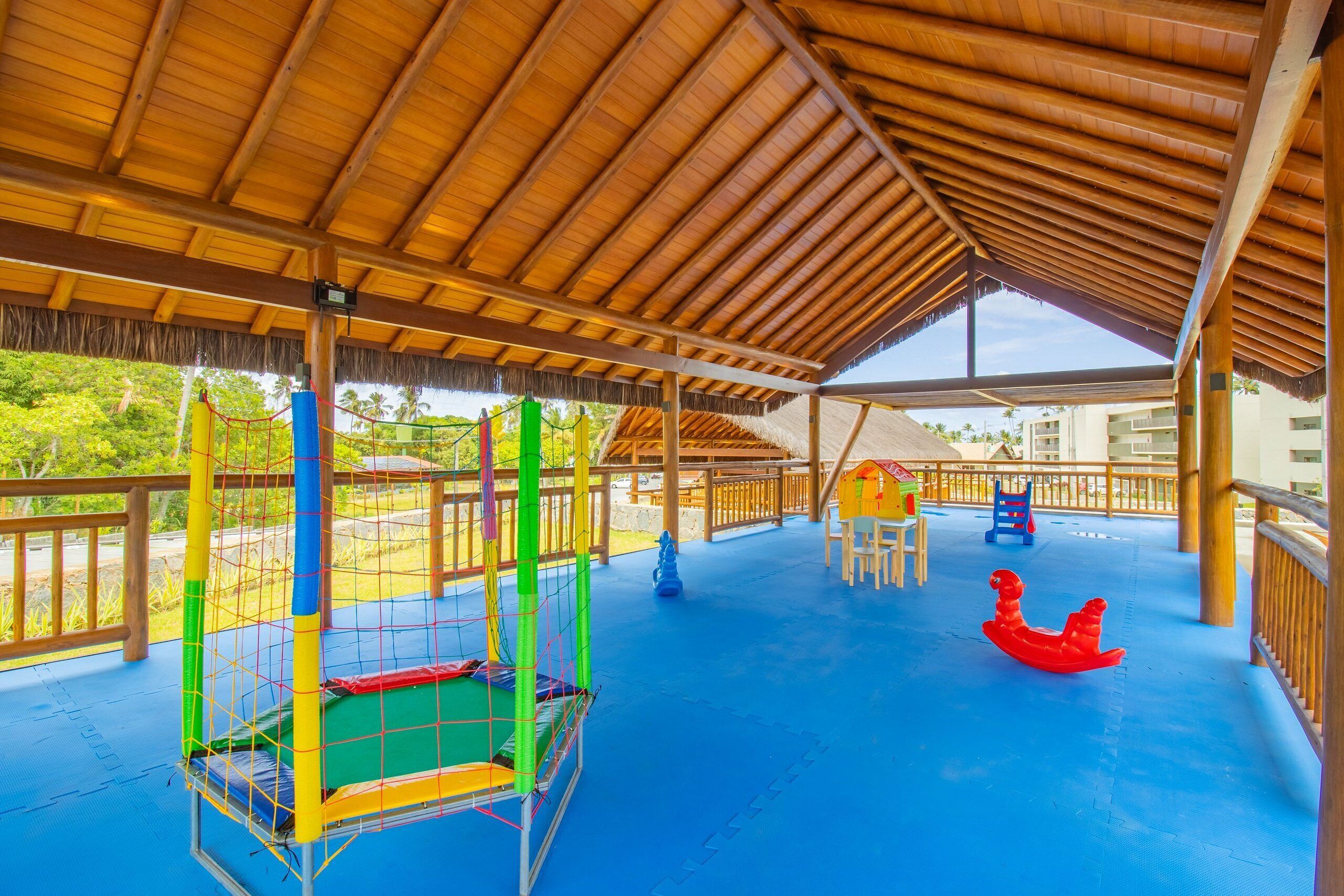 A covered outdoor play area with a blue floor, a netted play structure, and a red rocking horse.