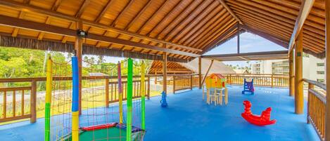 A covered outdoor play area with a blue floor, a netted play structure, and a red rocking horse.