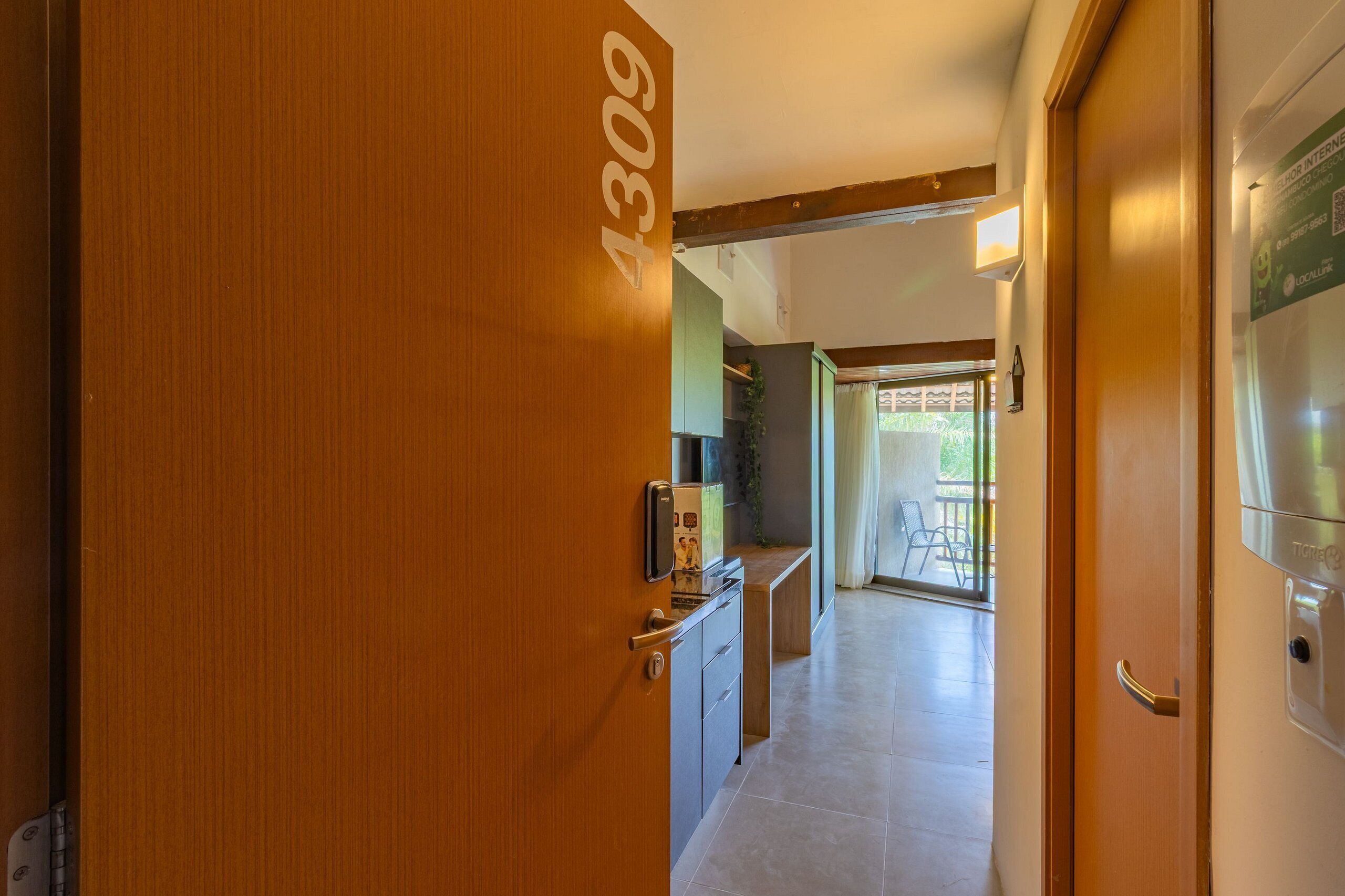 Un corridoio con una porta in legno con la scritta '4309' che conduce a una stanza con angolo cottura e vista su un patio esterno.