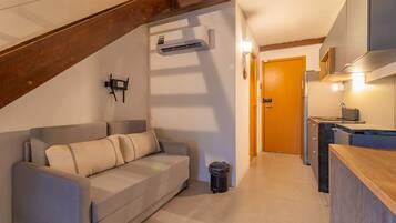 A compact living space with a sofa, a trash bin, a kitchenette, and a wooden staircase.