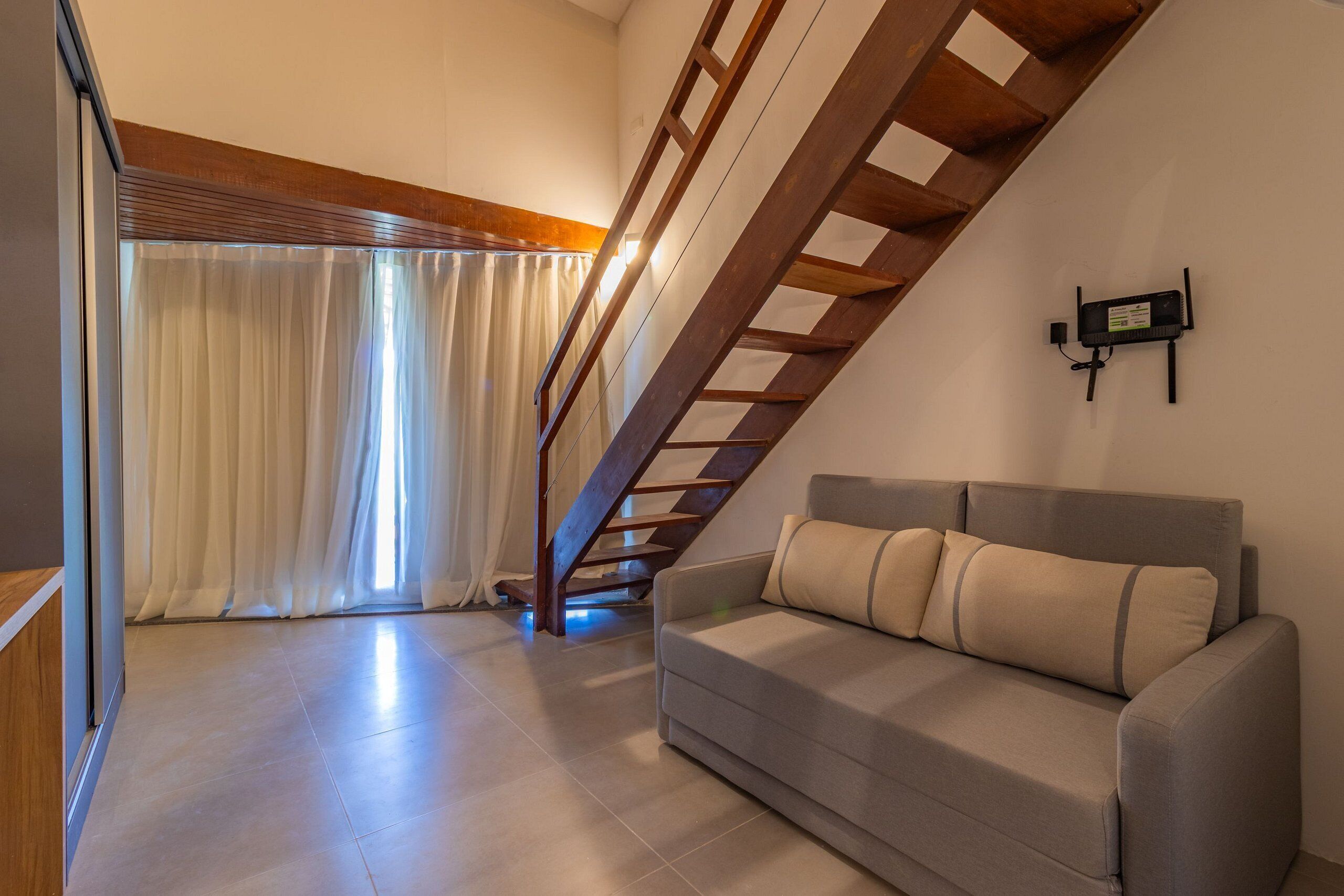 A modern living room with a grey sofa, wooden staircase, and a wall-mounted TV.