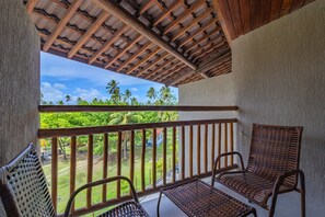 Un balcon doté de balustrades en bois, de meubles en osier et offrant une vue sur un paysage verdoyant parsemé de palmiers.