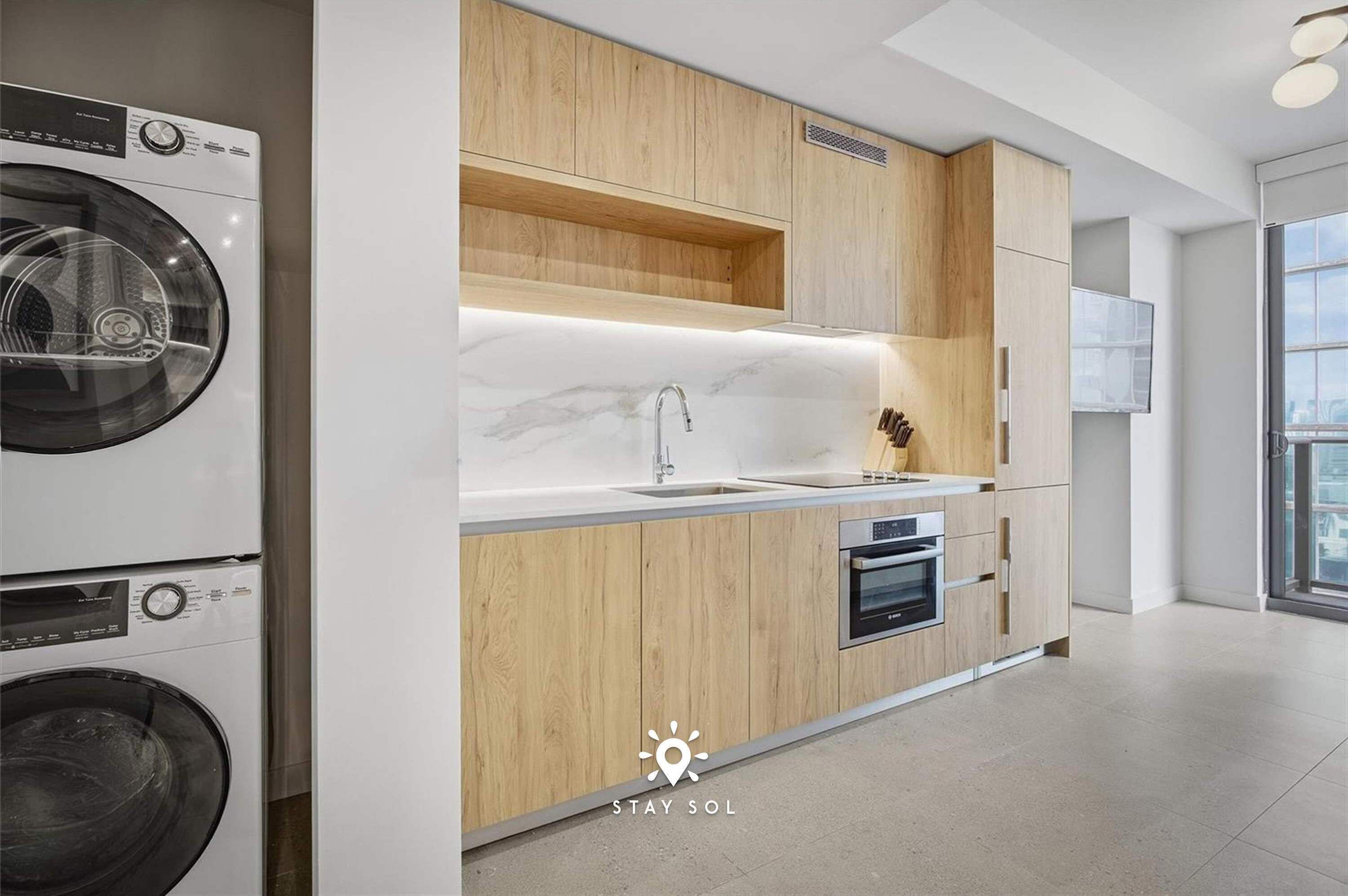 Een moderne keuken met houten kasten, een ingebouwde wasmachine en een groot raam.