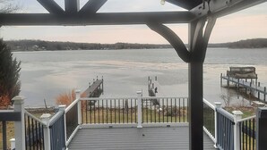 A covered deck with a view of a calm lake and distant shoreline. - A peaceful getaway awaits at this beautiful Log Home located on Sodus Bay (Wolcott)