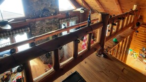 A wooden interior with a stone wall, wooden beams, and a balcony with a view. - A peaceful getaway awaits at this beautiful Log Home located on Sodus Bay (Wolcott)