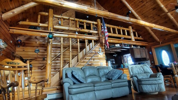 A log cabin interior with a wooden staircase, a sofa, and a rocking chair. - A peaceful getaway awaits at this beautiful Log Home located on Sodus Bay (Wolcott)