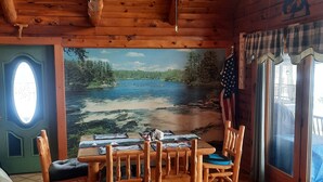 A wooden cabin interior with a dining table, chairs, a couch, and a mural of a lake. - A peaceful getaway awaits at this beautiful Log Home located on Sodus Bay (Wolcott)
