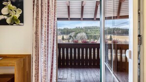 A balcony with a wooden floor, a patterned curtain, and a view of a forested landscape. - Speckhuisli – Mettmablick with Balcony, Breakfast, Sauna, Mountain View, Guesthouse (Grafenhausen)