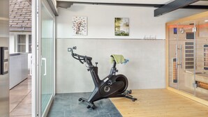 A modern gym with an exercise bike, a sauna, and a glass door leading to a patio area. - Speckhuisli – Mettmablick with Balcony, Breakfast, Sauna, Mountain View, Guesthouse (Grafenhausen)