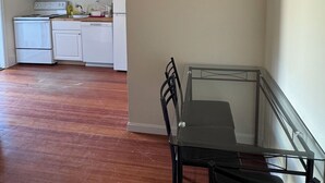 A room with a dining table and chairs, a kitchen area with white cabinets and appliances, and a wooden floor. - Updated 1BR apt, 1st floor, near T, free parking (Malden)